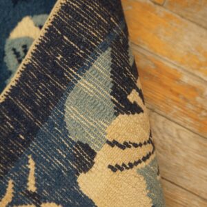 A rolled navy, teal, and beige patterned rug resting on distressed wood flooring.