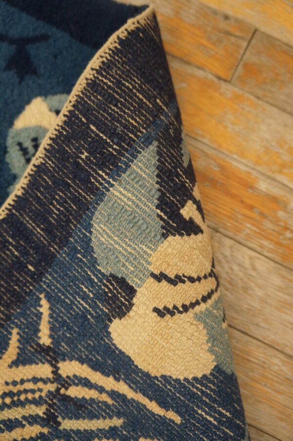 A rolled navy, teal, and beige patterned rug resting on distressed wood flooring.