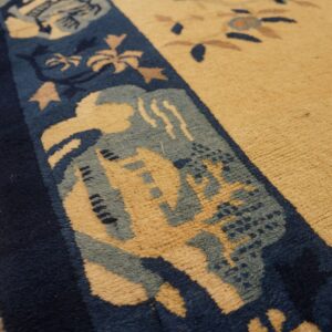 Textured tan rug field and complex blue border detail, photographed close-up on worn wooden flooring.