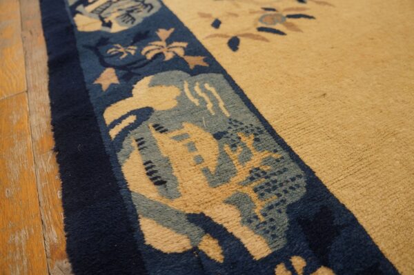 Textured tan rug field and complex blue border detail, photographed close-up on worn wooden flooring.