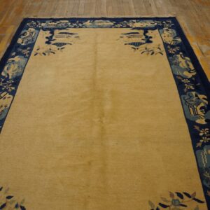 A golden area rug featuring a wide navy border with stylized blue and cream patterns rests on wooden floorboards.