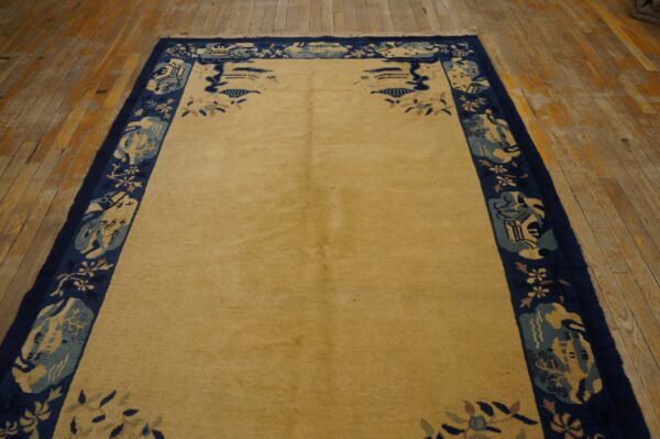 A golden area rug featuring a wide navy border with stylized blue and cream patterns rests on wooden floorboards.