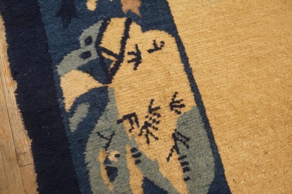 Detailed view of a tan, medium-pile rug border featuring dark blue, light blue, and abstract black motifs on wood flooring.