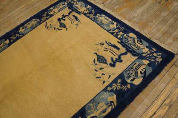 Low-pile gold rug features an intricate navy and blue pictorial border on rustic diagonal wood floors.