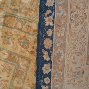 A close-up shows a tan and rust patterned rug field meeting a navy blue and floral patterned border.