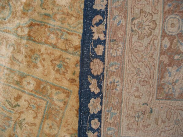 A close-up shows a tan and rust patterned rug field meeting a navy blue and floral patterned border.