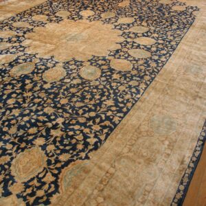 A large traditional rug in navy and tan with light blue accents rests on a brown wood floor.