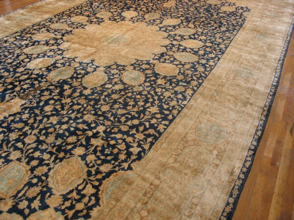 A large traditional rug in navy and tan with light blue accents rests on a brown wood floor.