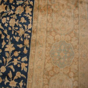 Navy blue and tan rug detail showing ornate floral patterns next to a wide border on wood flooring.