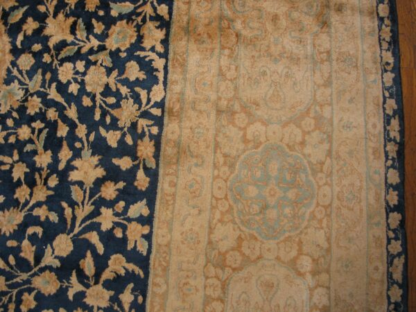 Navy blue and tan rug detail showing ornate floral patterns next to a wide border on wood flooring.