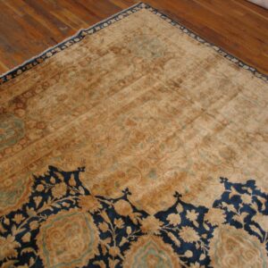 A low-pile gold and navy floral rug with teal accents rests on a warm, plank hardwood floor.