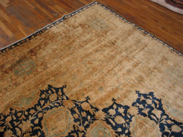 A low-pile gold and navy floral rug with teal accents rests on a warm, plank hardwood floor.