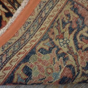 Close-up of a traditional patterned rug showing the low pile, orange edge binding, and the detailed, colorful foundation.