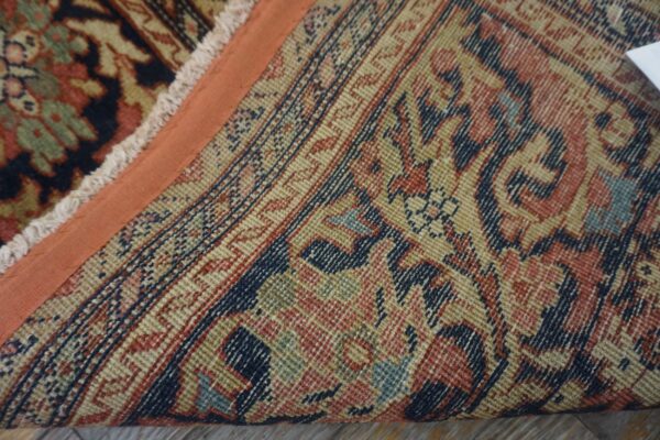Close-up of a traditional patterned rug showing the low pile, orange edge binding, and the detailed, colorful foundation.