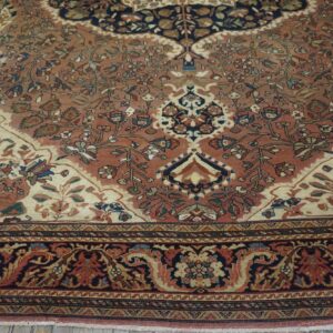 Intricate, low-pile rug featuring a rose and ivory field with navy and rust floral patterns over wood planks.