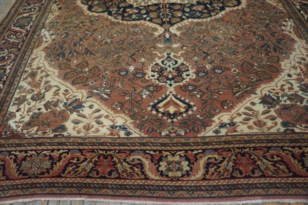 Intricate, low-pile rug featuring a rose and ivory field with navy and rust floral patterns over wood planks.