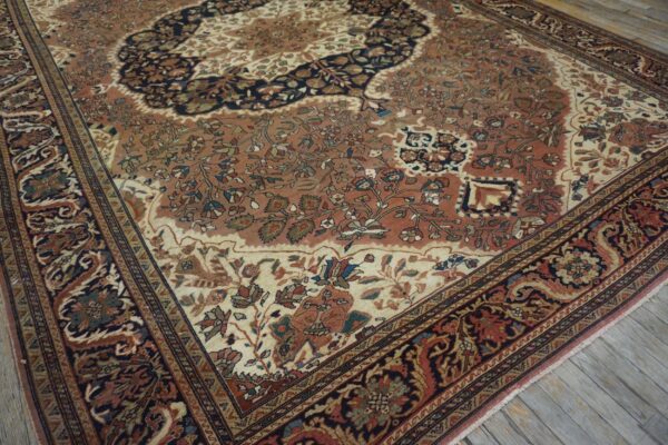 A traditional rug with rust, cream, and navy floral patterns rests on weathered gray wood flooring.