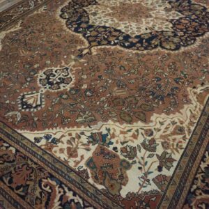 Traditional low-pile rug with rust, cream, and navy floral patterns on light wood floorboards.