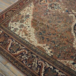 Detailed view of a traditional rug featuring terracotta, cream, and navy blue floral motifs on worn wood floors.