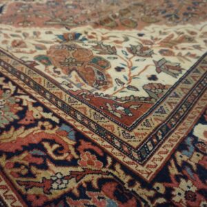 Intricate floral pattern features a cream center field meeting a dark blue and rust colored border.