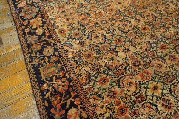Low-pile rug featuring a dense orange and blue pattern, dark border, resting on worn yellow wood flooring.