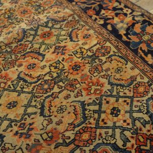 Detailed low-pile rug with geometric and floral motifs in beige, rust, and navy on wooden flooring.