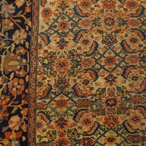 Close-up of a low-pile rug with dense orange, navy, and beige patterns, bordered by dark blue florals, on wood flooring.