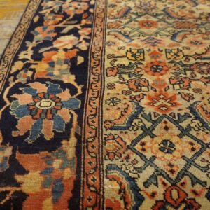 Navy bordered rug with complex orange and cream floral patterns rests on distressed wooden planks.