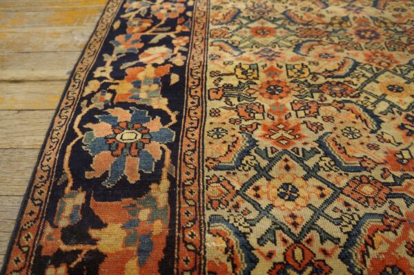 Navy bordered rug with complex orange and cream floral patterns rests on distressed wooden planks.