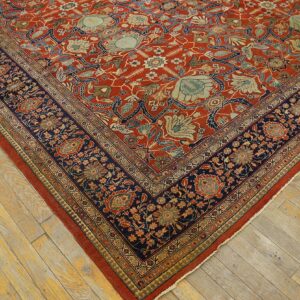 Red and navy patterned rug with complex floral motifs laid diagonally across worn wooden floorboards.