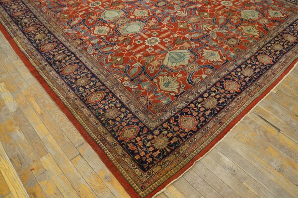 Red and navy patterned rug with complex floral motifs laid diagonally across worn wooden floorboards.