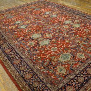 Traditional rust and navy floral rug displayed on wide, worn, light wood plank flooring.