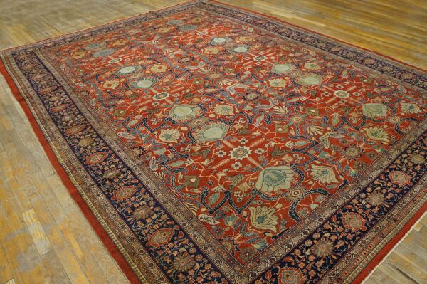 Traditional rust and navy floral rug displayed on wide, worn, light wood plank flooring.