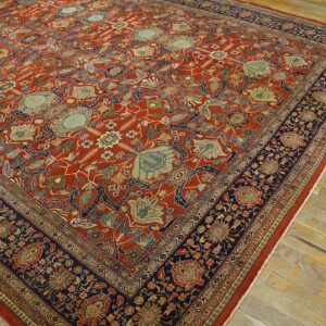 Intricate floral rug featuring a rust red field, light blue accents, and a wide navy border on worn wood floors.