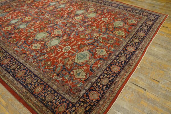 Intricate floral rug featuring a rust red field, light blue accents, and a wide navy border on worn wood floors.