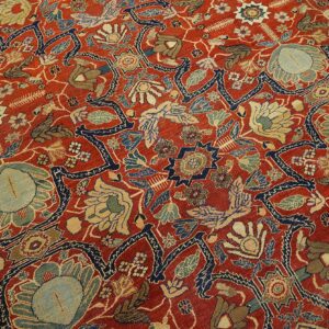 Detailed view of a low-pile rug with red field and dense floral patterns in navy, slate, and gold.