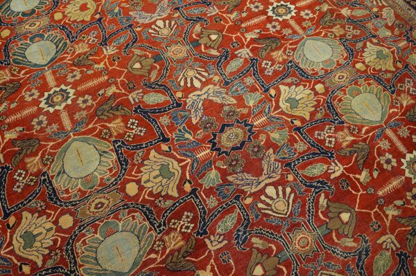 Detailed view of a low-pile rug with red field and dense floral patterns in navy, slate, and gold.