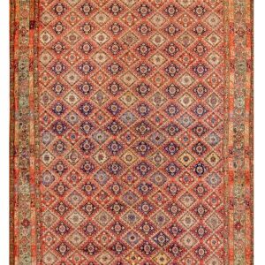 A rectangular rug featuring a dense, repeating diamond pattern in salmon, indigo, cream, and pale green tones.