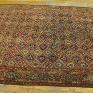 Rust and blue rug with a repeating geometric diamond trellis pattern and a detailed border, placed on wood planks.