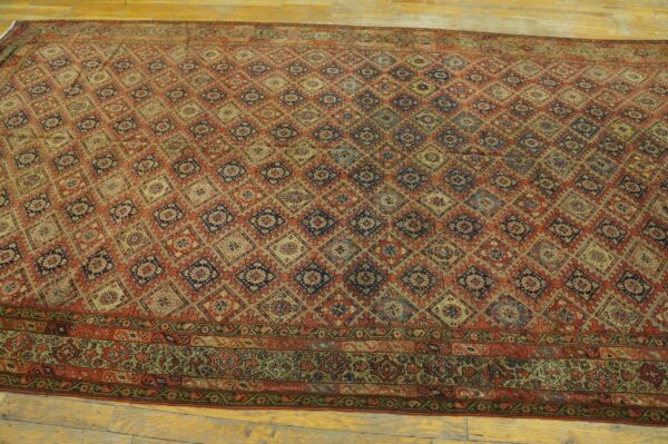 Rust and blue rug with a repeating geometric diamond trellis pattern and a detailed border, placed on wood planks.