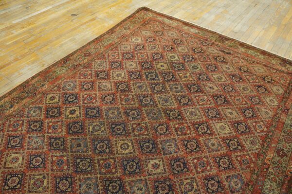 Repeating square geometric rug in terracotta, navy, and tan on distressed plank hardwood flooring.