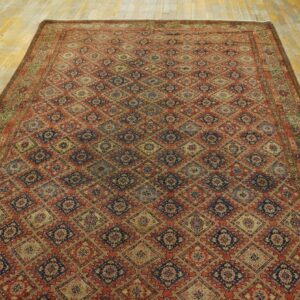 Intricate red and navy diamond patterned rug displayed on worn yellow wood floor planks.