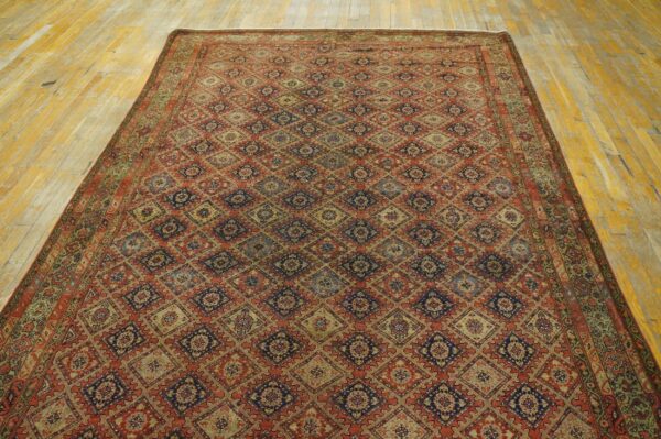 Intricate red and navy diamond patterned rug displayed on worn yellow wood floor planks.