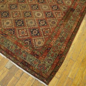 Red and tan rug with repeating square motifs and a detailed border rests on distressed wood flooring.