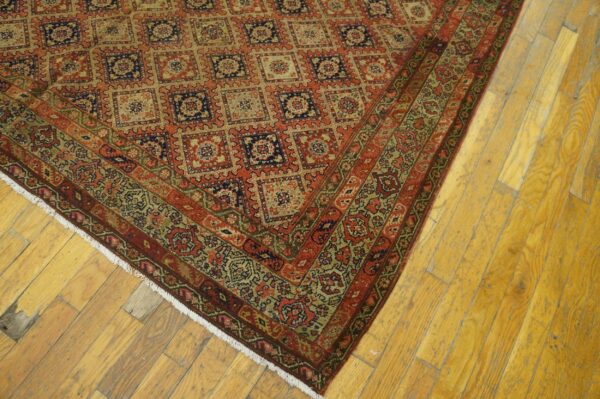 Red and tan rug with repeating square motifs and a detailed border rests on distressed wood flooring.