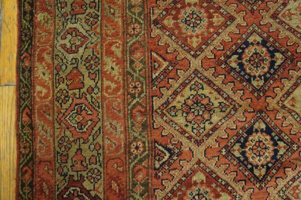 Detailed low-pile rug in rust, olive, and navy featuring repeating diamond patterns on light wood flooring.