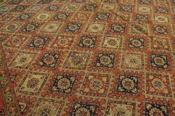 Rustic orange rug with a repeating lattice pattern of navy blue and beige serrated geometric medallions.