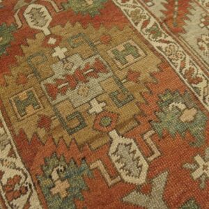 This close-up shows a rug with rust, tan, and green geometric tribal patterns and a distinct border.