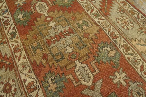 This close-up shows a rug with rust, tan, and green geometric tribal patterns and a distinct border.