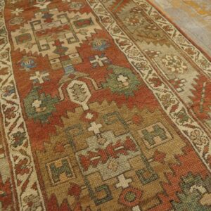Close-up of a low-pile runner rug with geometric motifs in rust, tan, and blue on aged wooden floorboards.